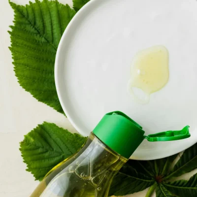 Flacon d’huile végétale bio et crème naturelle présentés avec des feuilles vertes sur fond clair